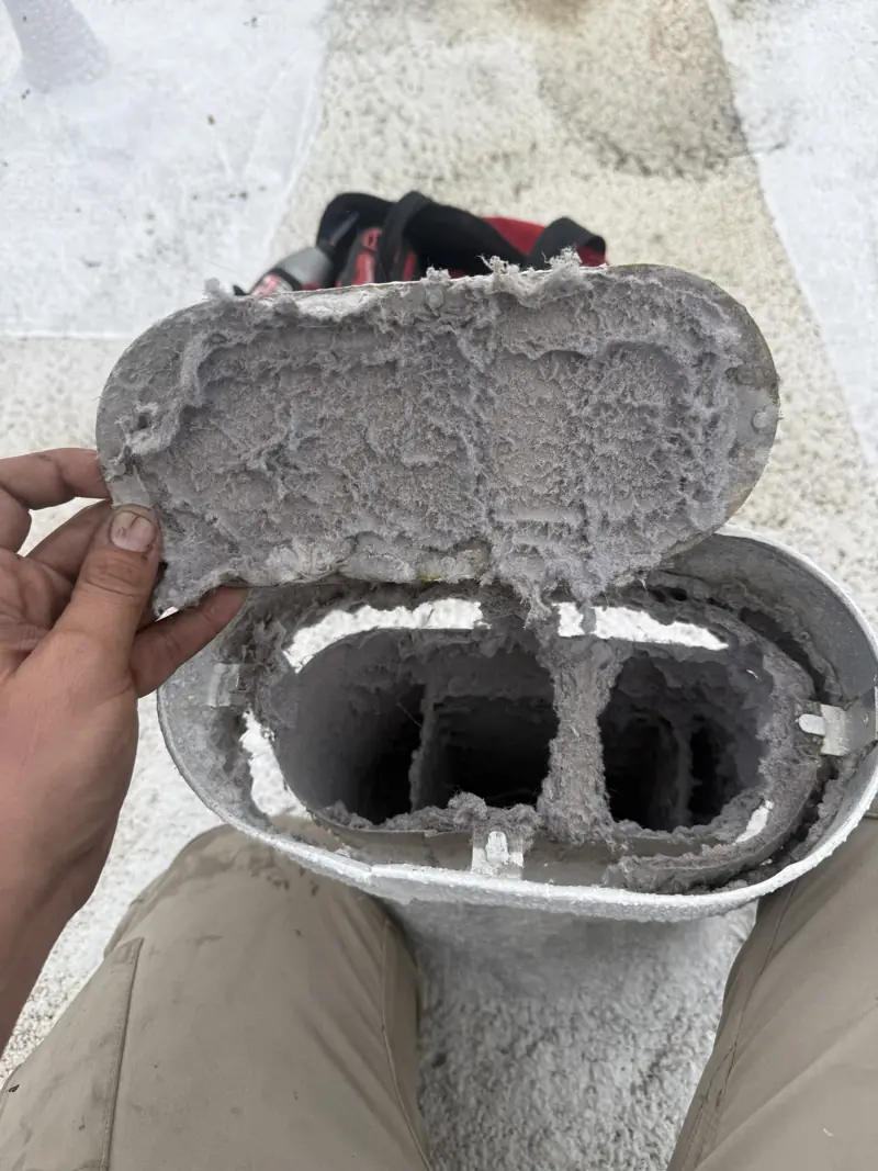 Technician opening a lint-clogged rooftop dryer vent hood